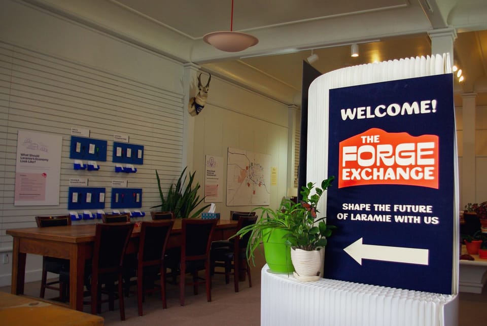 Image of the indoor Forge Exchange space with tables and chairs, informational displays, and interactive activities. 