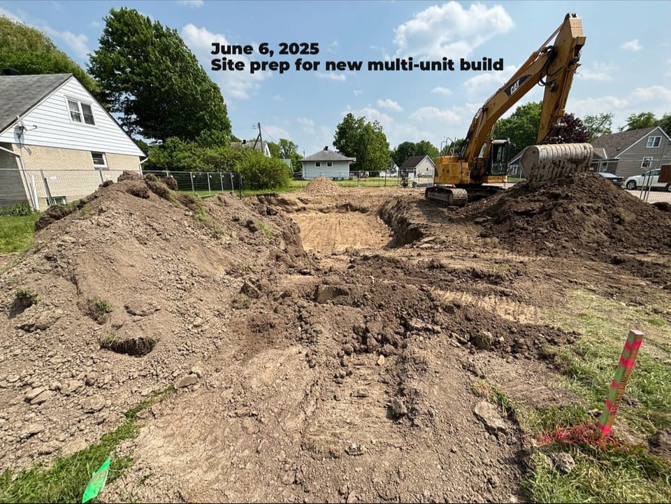 piece of equipment moving dirt in a fence yard to prepare site for additional work, mounds of dirt with a hole in the middle