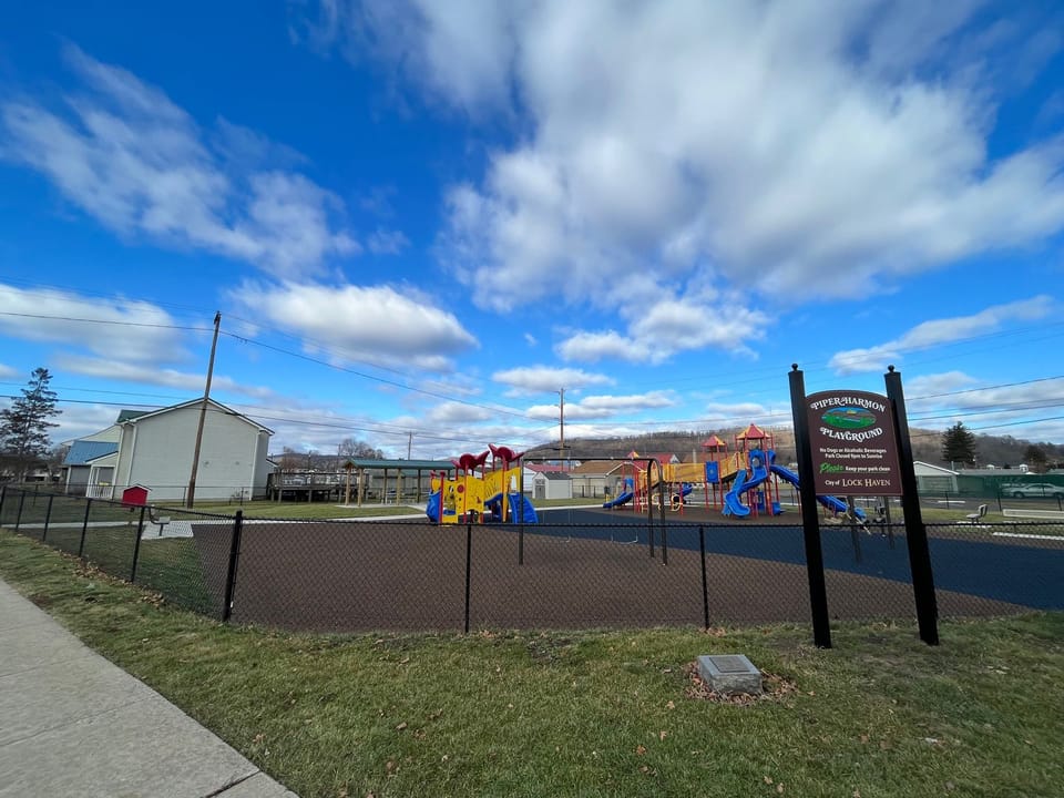 Image showing the Piper-Harmon Playground completed after construction. The image features an updated sign for the playground an shows the play equipment, new fall surface, and pavilion in the background.