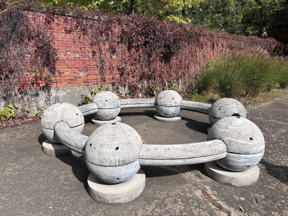a large circular concrete sculpture, 12’ in diameter, which includes an opening and a series of globes that invite visitors to sit or engage with the art 