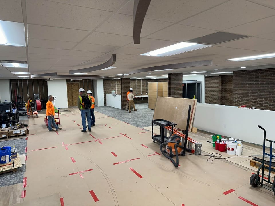 Image of the library first floor with ceiling in place and ceiling baffles being installed, several carpenters and other staff at work