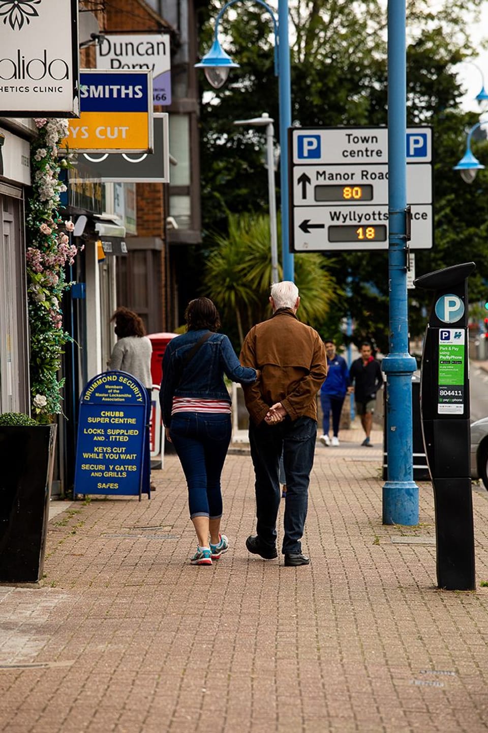 Image shows a man and a woman walking beside shops in Darkes Lane in Potters Bar.