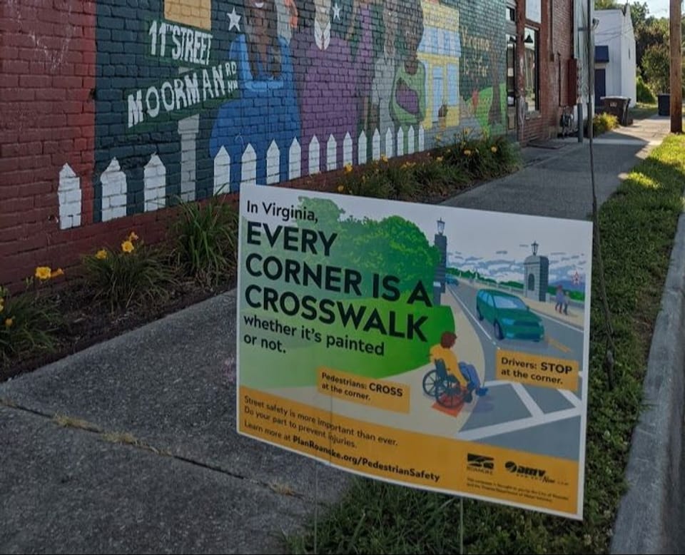 Image shows a "Every corner is a crosswalk" yard sign along a neighborhood street