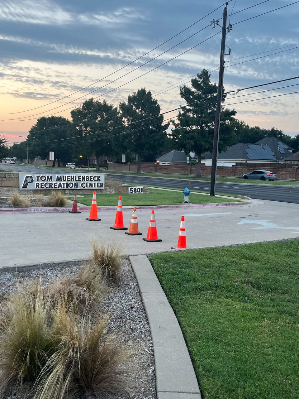 driveway entrance with orange and white construction cones surrounded by grass and landscaping 