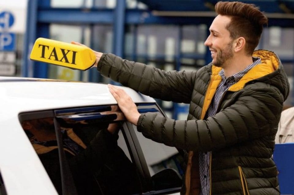 A man places a taxi sign on the roof of a vehicle