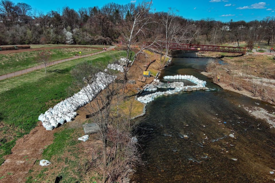 Photo of the Roanoke River flowing under the pedestrian bridge by Wasena Park. There is an enclosure made of sandbags in the river creating a construction site.