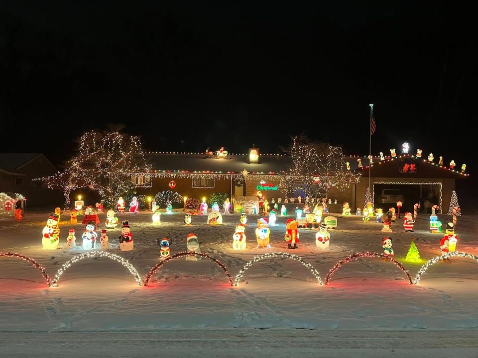 Festive suburban house adorned with bright Christmas lights, garlands, red bows, and a lit snowman in snowy yard, creating a warm holiday ambiance.