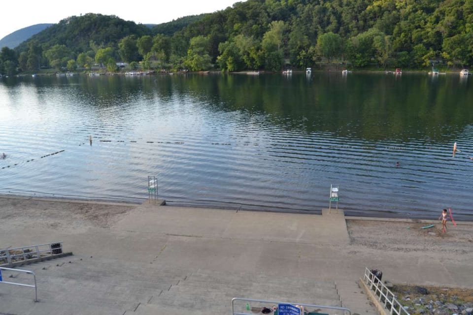 Picture of the City beach, with the shore in the foreground, two lifeguard stands, the Susquehanna river, and trees and mountains in the background.